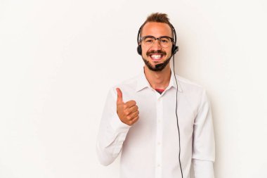 Beyaz arka planda izole edilmiş dövmeleri olan beyaz pazarlamacı genç adam gülümsüyor ve başparmağını kaldırıyor.