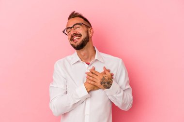 Pembe arka planda izole edilmiş dövmeleri olan genç beyaz bir adam. Gülüyor, elini kalbe koyuyor, mutluluk kavramını koruyor..