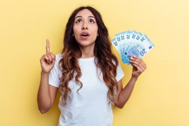 Sarı arka planda izole edilmiş banknotları tutan genç, melez bir kadın ağzı açık bir şekilde üst tarafı işaret ediyor..