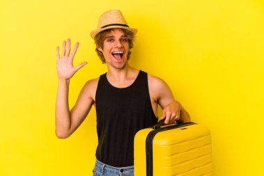 Makyajlı genç beyaz adam sarı arka planda tek başına seyahat edecek gülümseyerek beş numarayı parmaklarıyla gösterecek..