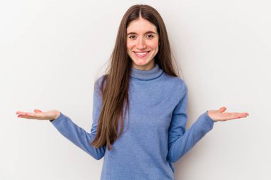 Beyaz arka planda izole genç beyaz kadın kollarıyla ölçek yapar, mutlu ve kendinden emin hisseder..