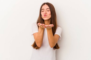 Beyaz arka planda izole edilmiş genç beyaz bir kadın dudaklarını katlıyor ve hava öpücüğü yollamak için avuç içleri tutuyor..