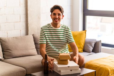 Genç melez adam pizza yiyor, burger yiyor ve bira içiyor.