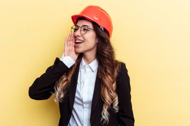 Genç mimar melez kadın sarı arka planda izole edilmiş bağırıyor ve avuç içini açık tutuyor..