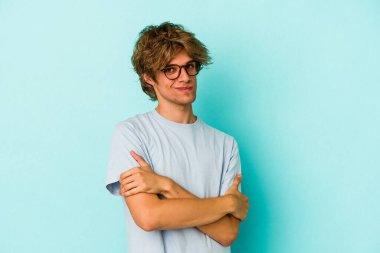 Makyajlı genç beyaz adam mavi arka planda izole edilmiş şüpheli, belirsiz, seni muayene ediyor..