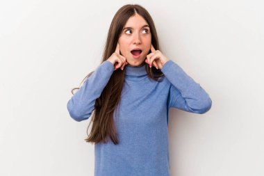 Beyaz arka planda izole edilmiş genç beyaz bir kadın parmaklarıyla kulaklarını kapatıyor, gürültülü bir ortam yüzünden stresli ve çaresiz..