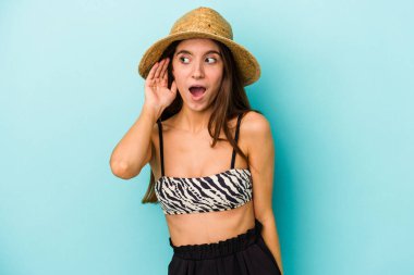 Genç beyaz bir kadın kumsala gidiyor. Mavi arka planda izole edilmiş bikini giyiyor. Dedikoduları dinliyor..