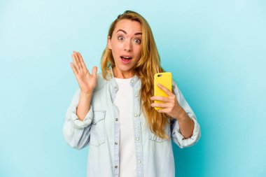 Mavi arka planda cep telefonu tutan beyaz kadın şaşırdı ve şok oldu..