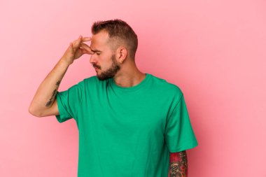 Pembe arka planda izole edilmiş dövmeleri olan, başı ağrıyan, yüzünün ön kısmına dokunan genç beyaz bir adam..