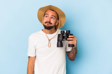 Mavi arka planda dürbün tutan beyaz dövmeli genç bir adam hedeflerine ve amaçlarına ulaşma hayali kuruyor.