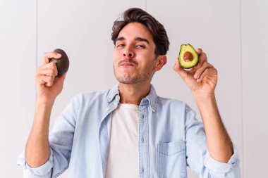 Genç melez adam mutfağında avokado tutuyor.