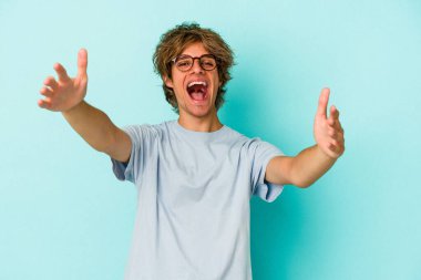 Mavi arka planda izole edilmiş beyaz makyajlı genç bir adam kameraya sarıldığı için kendinden emin..