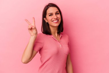 Genç beyaz kadın pembe arka planda izole edilmiş neşeli ve kaygısız parmakları olan bir barış sembolü gösteriyor..