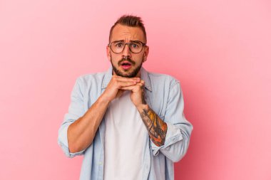 Pembe arka planda izole edilmiş beyaz dövmeli genç bir adam şans için dua ediyor, şaşırıyor ve ağzını açıyor..