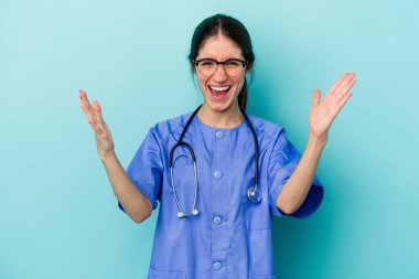 Kafkasyalı genç hemşire mavi arka planda izole edilmiş. Hoş bir sürprizle karşılaşıyor, heyecanlı ve el kaldırıyor..