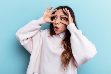 Mavi arka planda izole edilmiş genç Meksikalı kadın bir başarı fırsatı bulmak için gözlerini açık tutuyor..