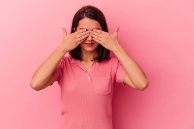 Pembe arka planda izole edilmiş genç beyaz kadın elleriyle gözlerini kapatmaktan korkuyor..