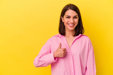Sarı arka planda izole edilmiş genç beyaz kadın gülümsüyor ve başparmağını kaldırıyor.
