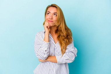 Beyaz kadın mavi arka planda izole edilmiş düşünüyor ve yukarı bakıyor, yansıtıyor, düşünüyor, hayal kuruyor..