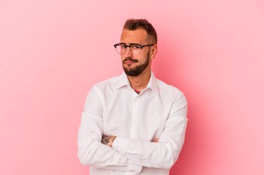 Pembe arka planda izole edilmiş beyaz dövmeli genç adam alaycı bir ifadeyle kameraya bakıyor..