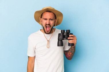 Mavi arka planda, elinde dürbün tutan beyaz dövmeli genç bir adam çok sinirli ve agresif bir şekilde bağırıyor..