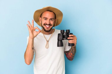 Elinde dürbün tutan beyaz bir genç adam mavi arka planda izole edilmiş neşeli ve kendinden emin..