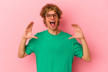 Pembe arka planda soyutlanmış beyaz makyajlı genç bir adam avuçlarıyla bir şey tutuyor ve kameraya sunuyor..