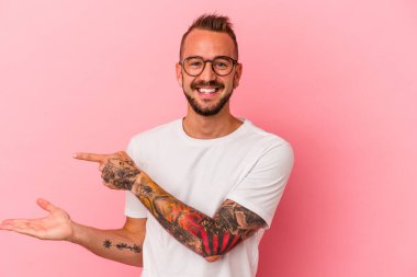 Pembe arka planda dövmeleri olan beyaz bir adam heyecanlı bir şekilde palmiye ağacında bir kopyasını tutuyor..