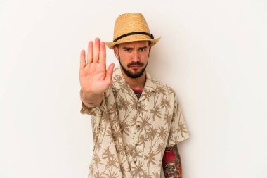 Beyaz arka planda izole edilmiş yazlık giysiler giyen, elini uzatmış, dur işaretini gösteren beyaz dövmeli genç beyaz bir adam..