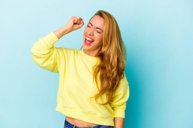 Mavi arka planda izole edilmiş beyaz kadın zaferi, tutkuyu ve coşkuyu kutluyor, mutlu bir ifade..