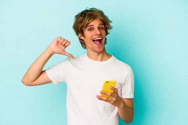 Jovem Caucasiano Com Maquiagem Segurando Celular Isolado Fundo Azul Sente — Fotografia de Stock