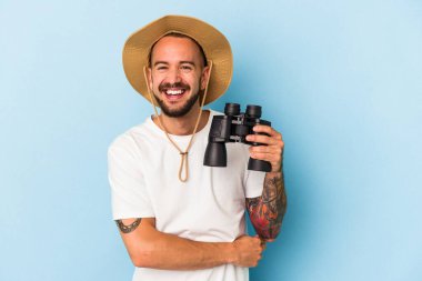 Mavi arka planda elinde dürbün tutan beyaz dövmeli genç bir adam gülüyor ve eğleniyor..