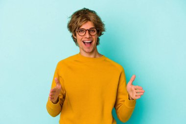 Mavi arka planda soyutlanmış beyaz makyajlı genç bir adam iki eliyle bir şey tutuyor..