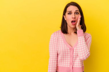 Sarı arka planda izole edilmiş genç beyaz kadın yüksek sesle bağırıyor, gözleri açık ve elleri gergin tutuyor..