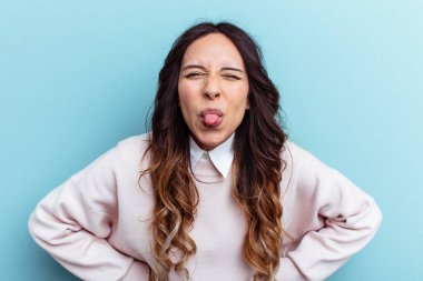 Mavi arka planda izole edilmiş genç Meksikalı kadın. Komik ve dost canlısı bir dil uzatıyor..