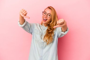 Beyaz tenli sarışın kadın pembe arka planda izole edilmiş. Baş parmağını kaldırıyor, gülümsüyor ve kendinden emin..