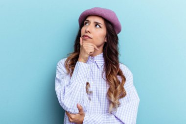 Genç Meksikalı kadın mavi arka planda izole edilmiş düşünüyor, bakıyor, yansıtıyor, düşünüyor, hayal kuruyor..