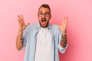 Pembe arka planda dövmeleri olan beyaz bir adam zaferi ya da başarıyı kutluyor, şaşırıyor ve şok oluyor..