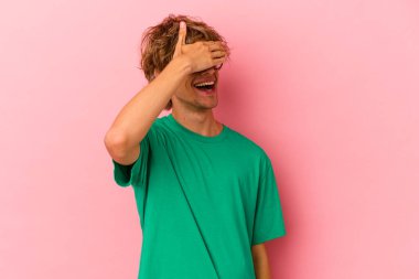 Pembe arka planda soyutlanmış beyaz makyajlı genç bir adam elleriyle gözlerini kapatıyor, gülümseyerek bir sürpriz bekliyor..