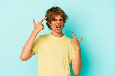 Mavi arka planda soyutlanmış beyaz makyajlı genç bir adam işaret parmağıyla hayal kırıklığı jesti yapıyor..