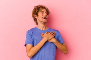 Pembe arka planda soyutlanmış beyaz makyajlı genç bir adam gülüyor, ellerini yüreğine koyuyor, mutluluk kavramını koruyor..