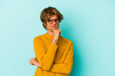 Makyajlı genç beyaz adam mavi arka planda izole edilmiş düşünüyor ve yukarı bakıyor, yansıtıyor, düşünüyor, hayal kuruyor..