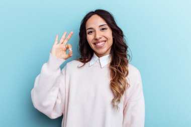Mavi arka planda izole edilmiş genç Meksikalı kadın neşeli ve kendinden emin, iyi bir jest yapıyor..