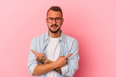 Pembe arka plan noktalarına izole edilmiş beyaz dövmeli genç bir adam iki seçenek arasında seçim yapmaya çalışıyor..