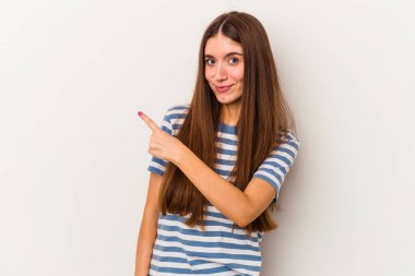 Beyaz arka planda izole edilmiş genç beyaz bir kadın gülümsüyor ve boş alanda bir şeyler gösteriyor..