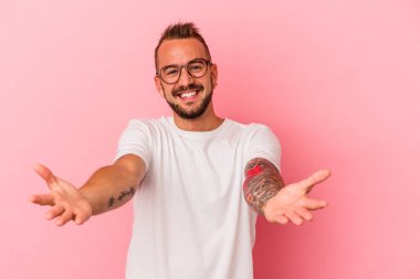 Pembe arka planda izole edilmiş dövmeleri olan beyaz bir genç hoş bir ifade sergiliyor..