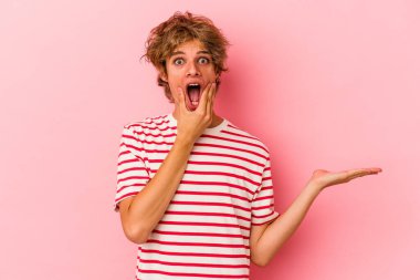 Pembe arka planda izole edilmiş beyaz makyajlı genç bir adam bir avuç içinde fotokopi alanı tutuyor, el üstünde tutuyor. Şaşırmış ve mutlu..