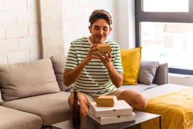 Genç melez adam pizza yiyor, burger yiyor ve bira içiyor.