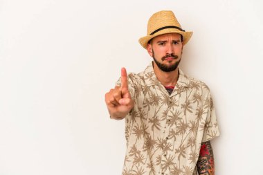 Beyaz arka planda izole edilmiş yazlık giysiler giyen beyaz dövmeli genç beyaz bir adam parmak ile bir numarayı gösteriyor..