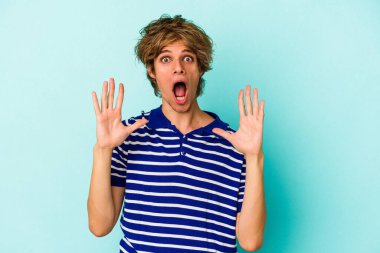 Makyajlı genç beyaz adam mavi arka planda izole edilmiş gökyüzüne haykırıyor, yukarı bakıyor, hayal kırıklığına uğramış..